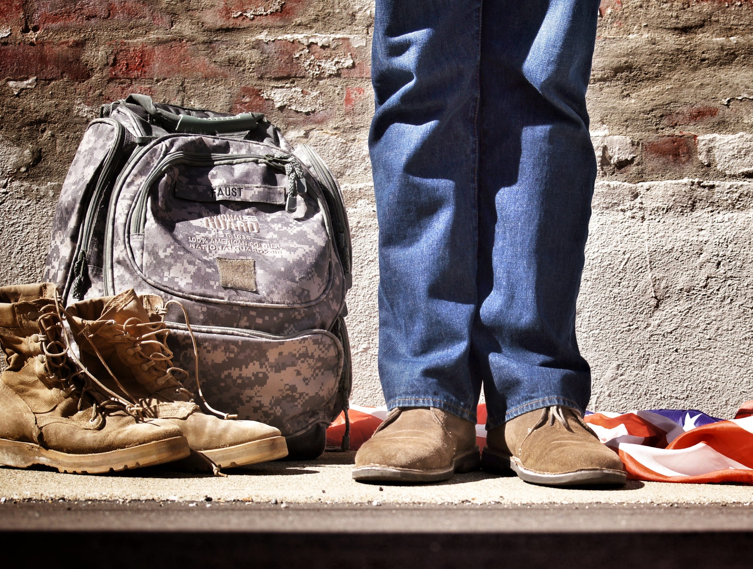 militaru veteran standing next to boots, backpack and American flag