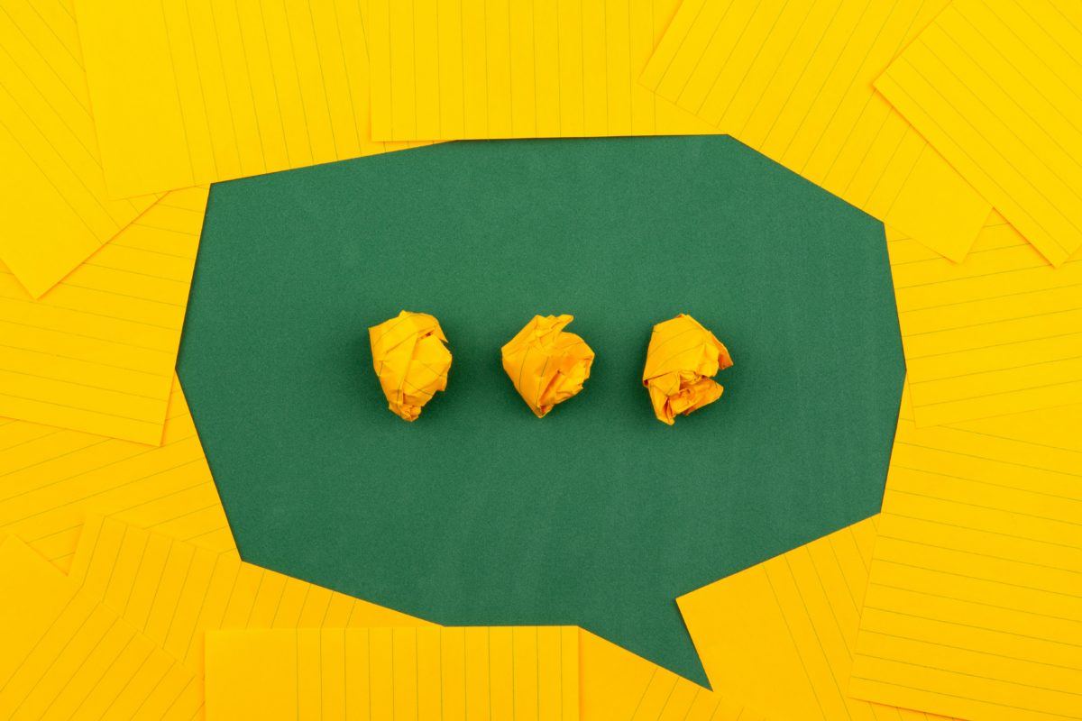 A speech bubble made out of green and yellow paper. The bubble is green and has three dots in it.