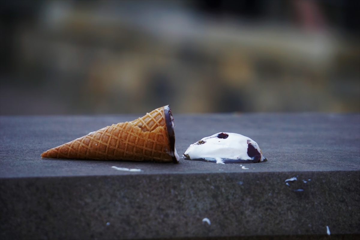 A sugar cone lays on the concrete, the ice cream has fallen out of the cone.