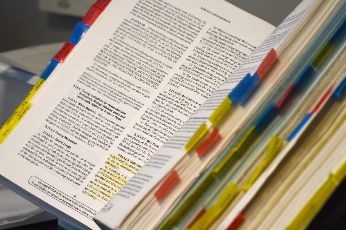 A dense textbook lays open. Dispersed through the pages are red, blue, and yellow tabs.