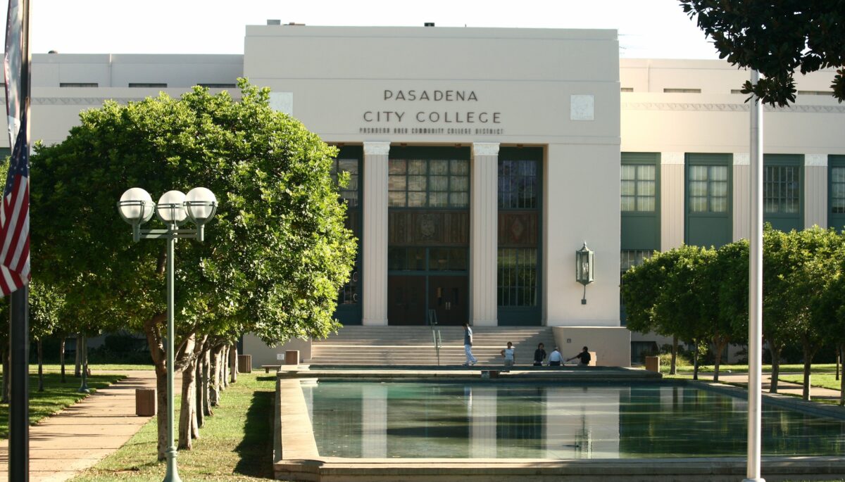 A large white building that says "Pasadena City College" on the front. In front of the building is a large fountain and rows of trees.
