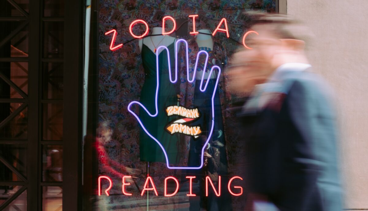 Two men walk past a neon sign that says "Zodiac Reading"