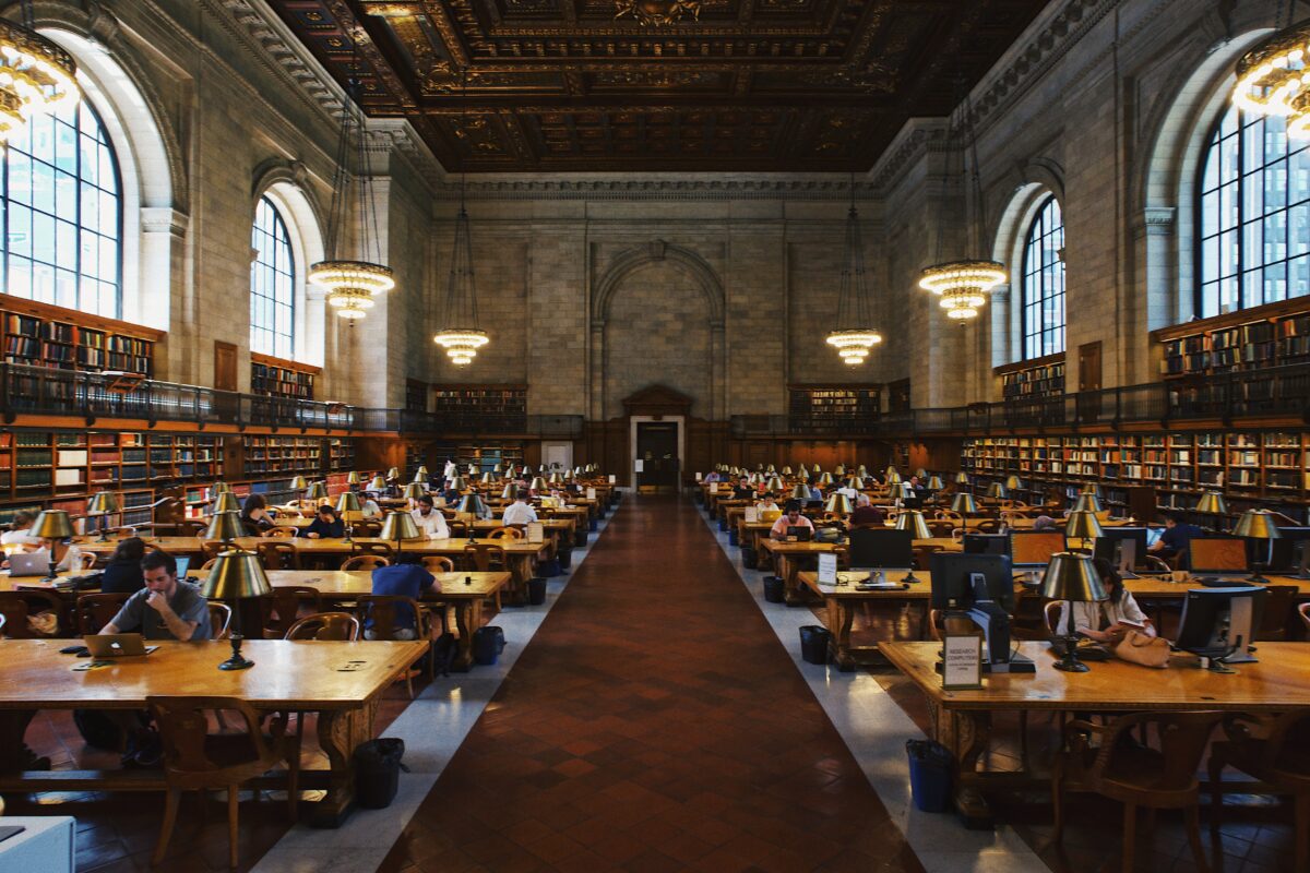 A large historic library with stone walls and long wooden tables with students sitting at them.