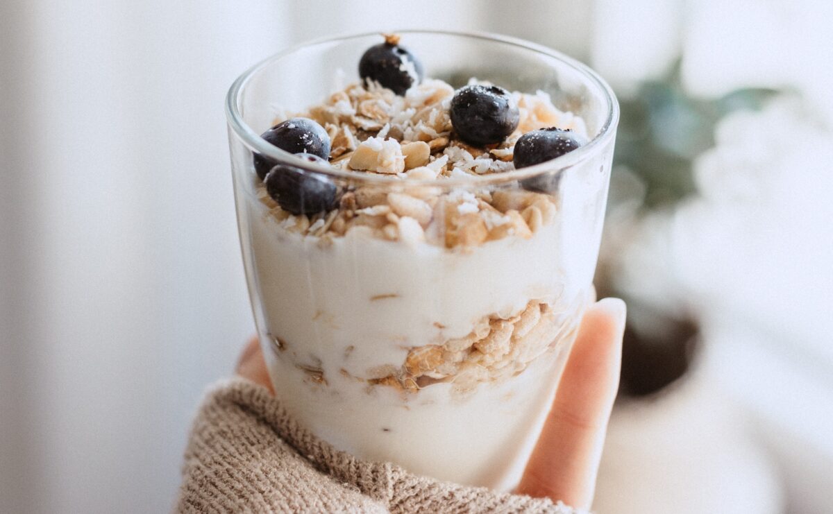 A hand holds a glass filled with yogurt, oatmeal, and blueberries.