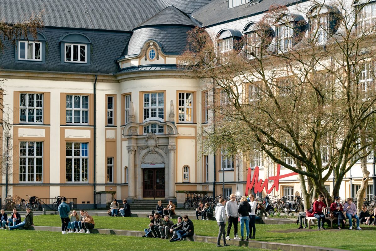 Students sit on a quad in front of a large school building.