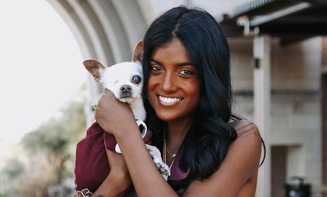 Ella, a young woman with brown skin and black hair, holds a small white dog up to her face. She wears a sparkly gold dress and red graduation sash.