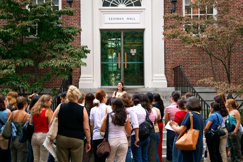A tour guide stands on a set of stairs facing her tour group.