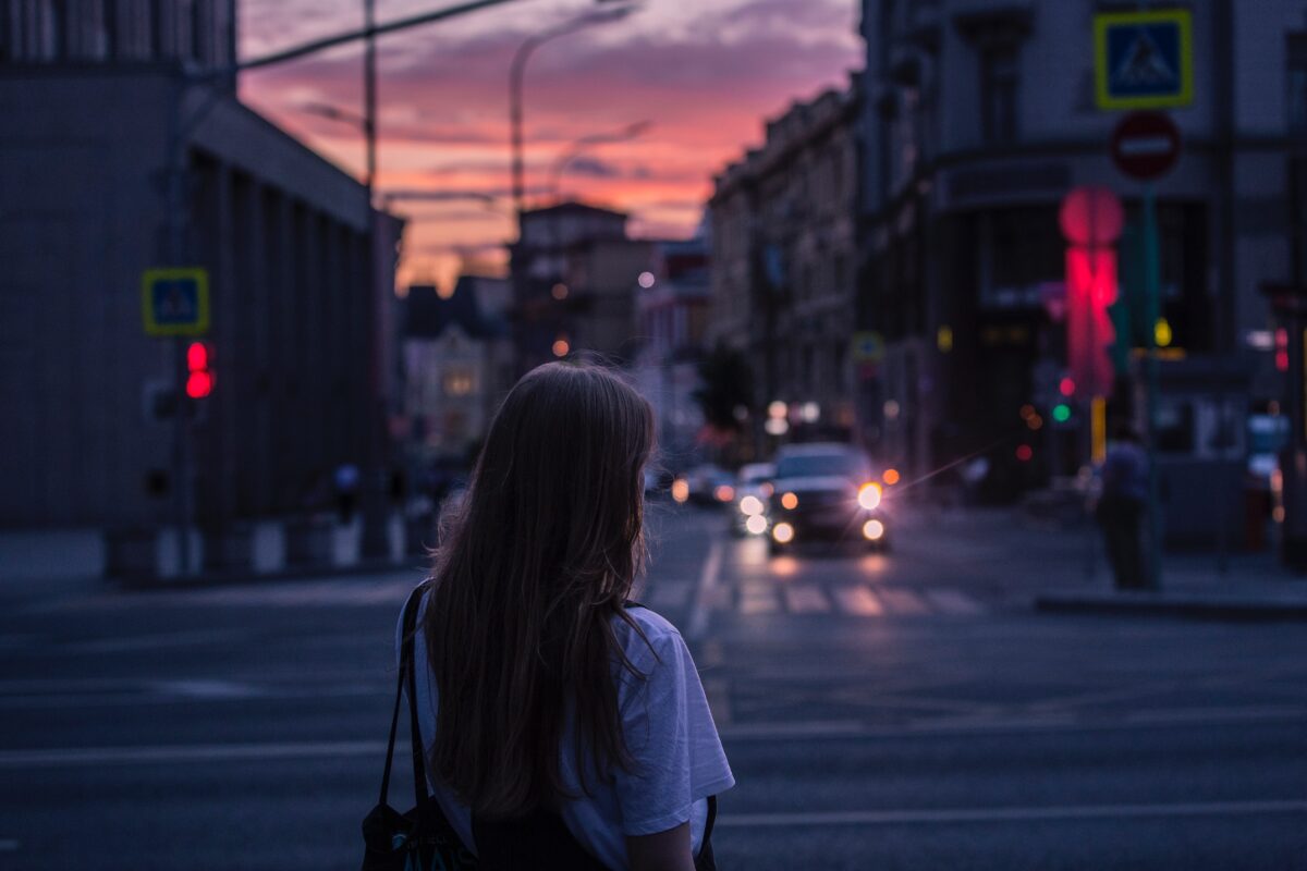 A girl stands in front of an intersection at sunset.