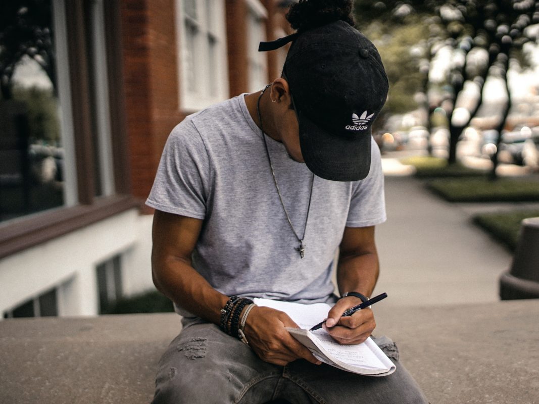 A student sitting outside on a ledge taking notes on a notepad.