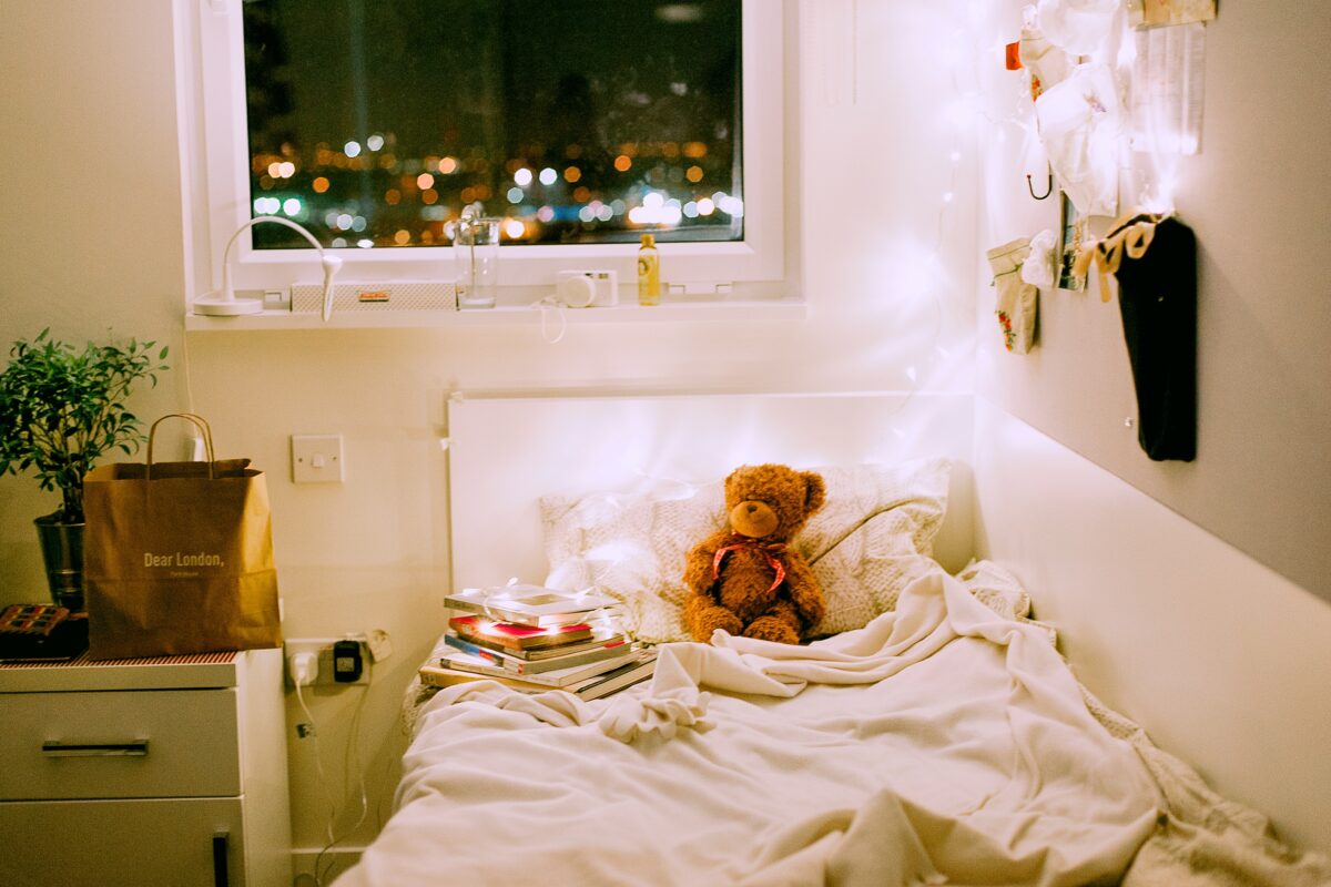 A cozy bed with a teddy bear on it.