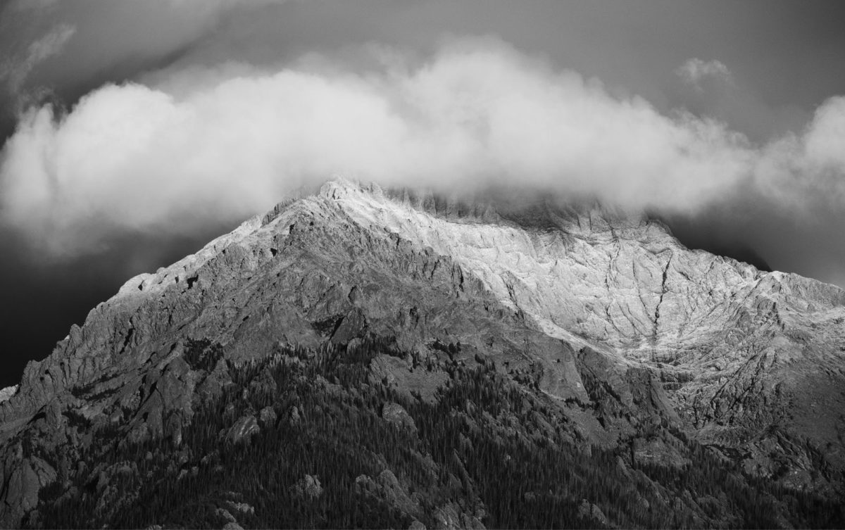 A black and white photo of a mountain with clouds over top.