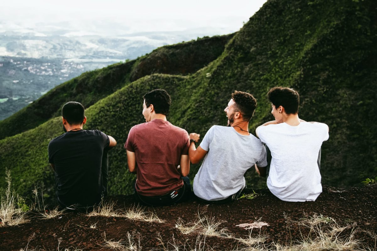 Four young men sit on a ledge overlooking a view of a grassy mountain.