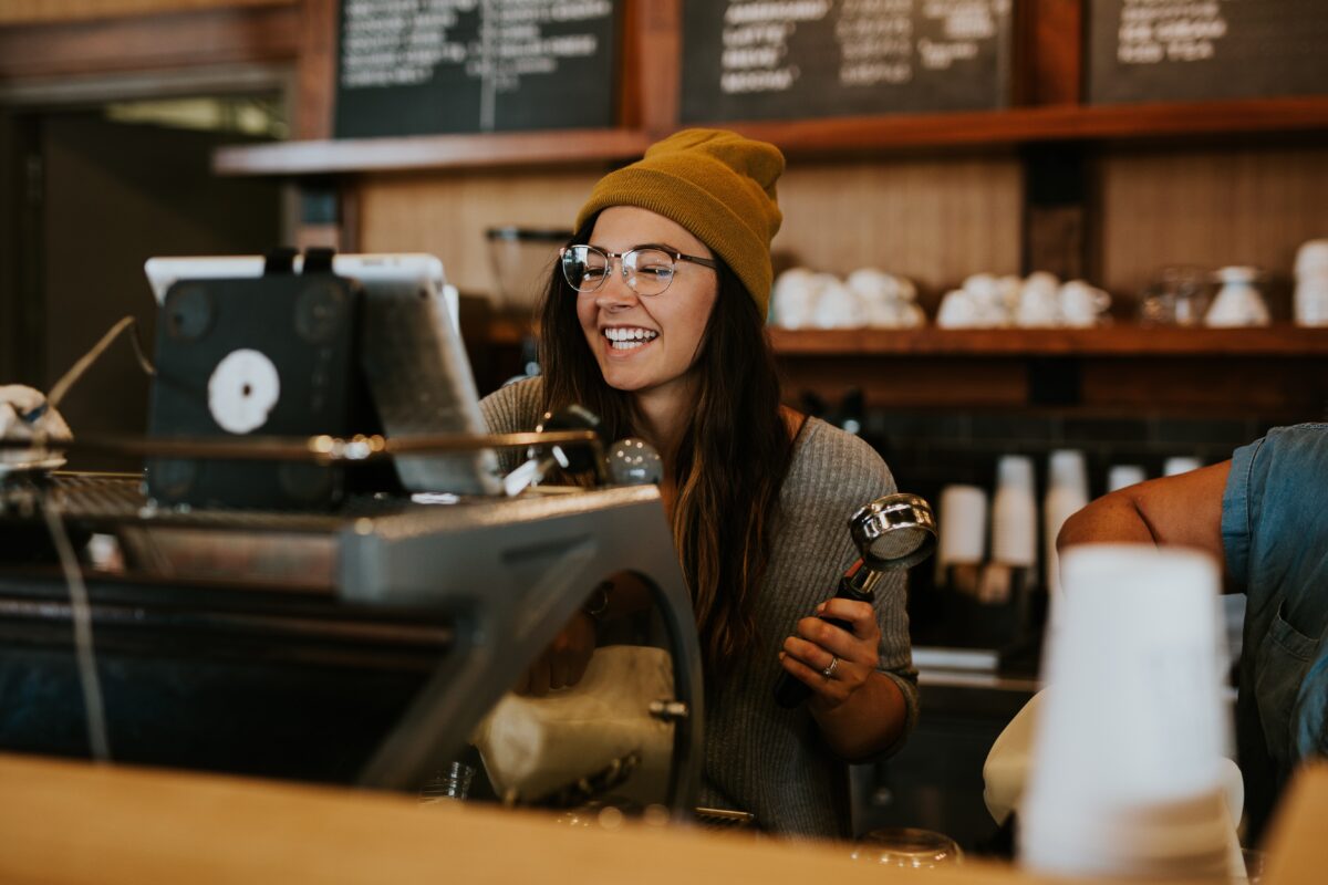 A smiling young woman works behind the counter at a coffee shop.