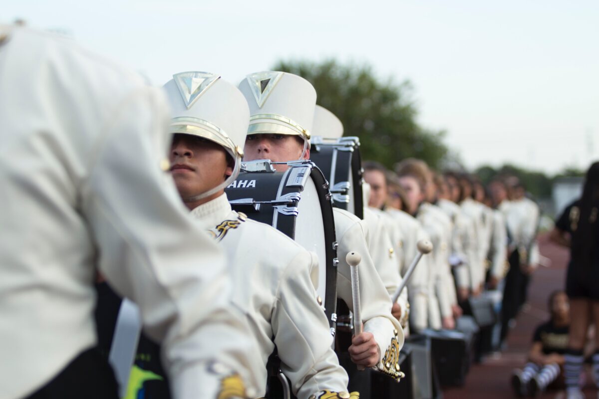  A line of drummers in white marching band uniforms.